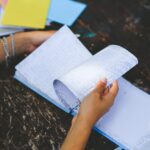 Dłonie przekartkowują papierowy notatnik na starym drewnianym stole na zewnątrz