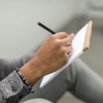 Dorosła osoba pisze ołówkiem w papierowym dzienniku rozwoju osobistego