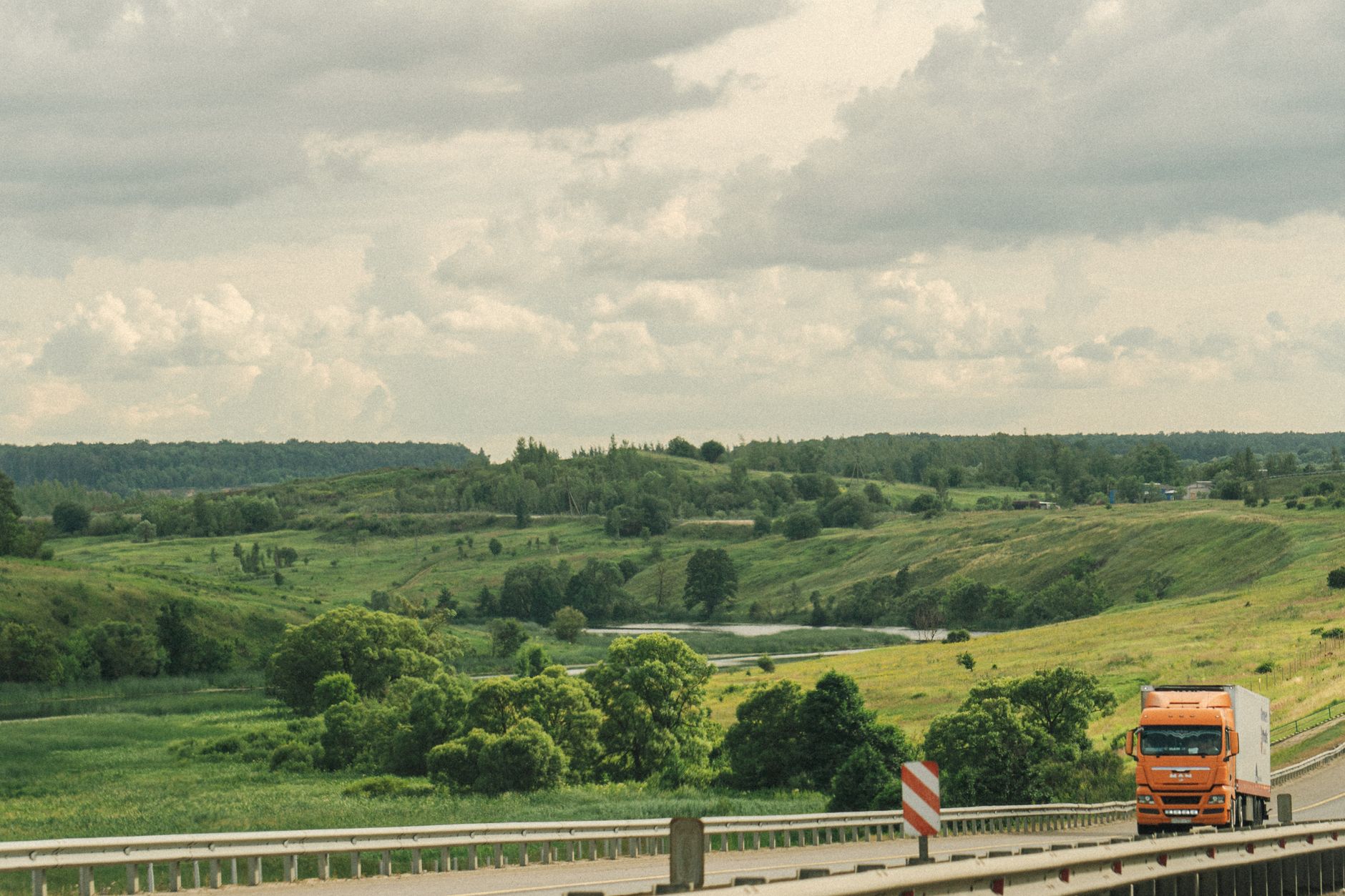 Pomarańczowa ciężarówka na autostradzie wśród zielonych pagórków