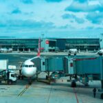 Samolot pasażerski przy rękawie lotniczym obsługiwany przez pojazdy cargo