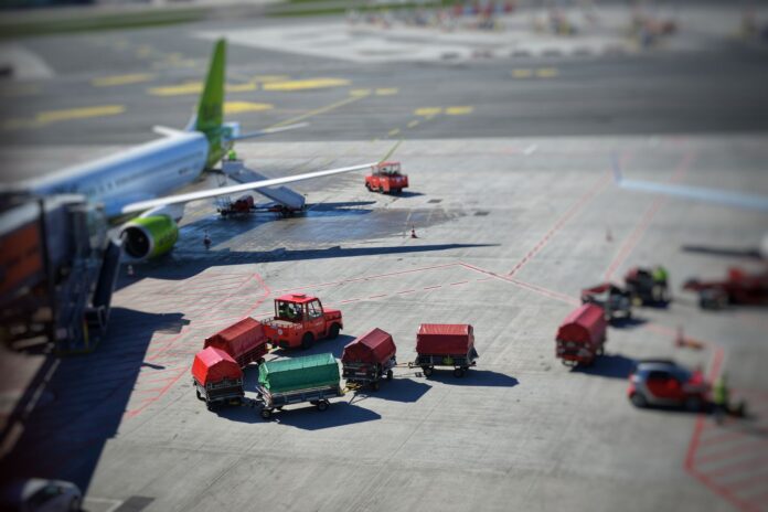 Samolot cargo na płycie lotniska z wózkami bagażowymi w słońcu