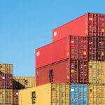 Kolorowe, piętrowo ułożone kontenery shippingowe pod błękitnym niebem