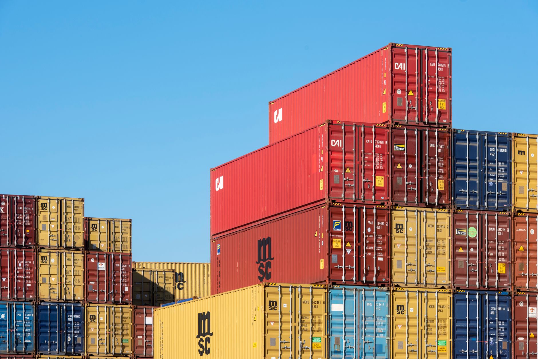 Kolorowe, piętrowo ułożone kontenery shippingowe pod błękitnym niebem